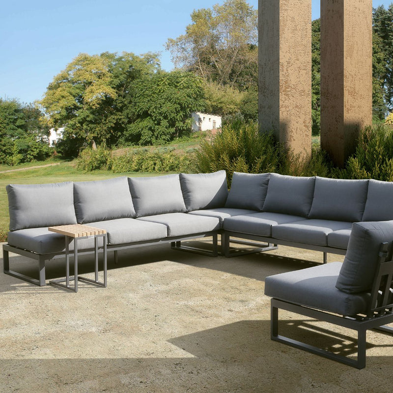 Aluminium 7-seater modular outdoor furniture, Denver lounge set in charcoal, adaptable for balcony or courtyard, set outdoors against lush greenery and rustic building.
