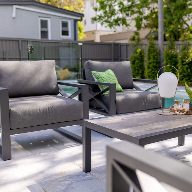Outdoor furniture collection featuring aluminium armchairs and sofa in charcoal, part of the Linear Lounge set by the pool.