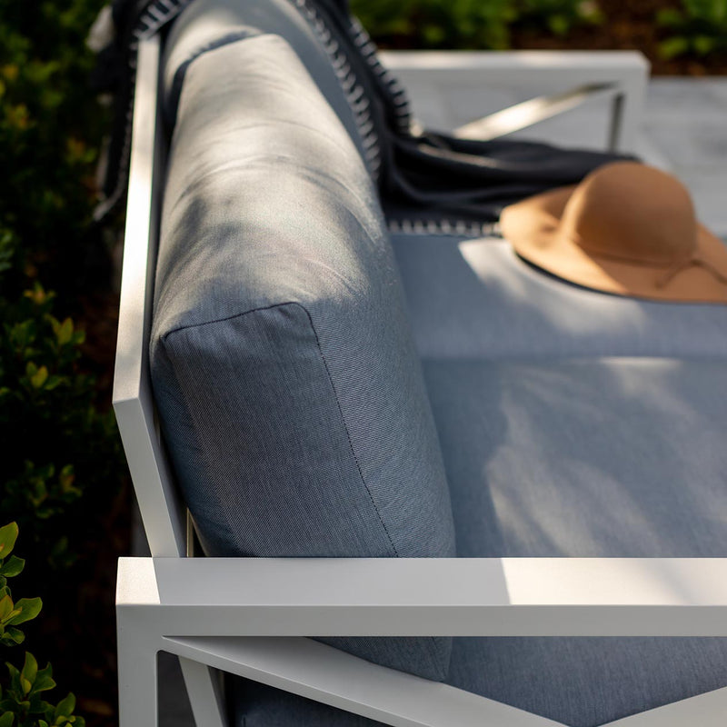 Aluminium outdoor furniture from Linear Lounge collection, featuring a 2-seater outdoor lounge with white frame, light grey cushions, and a brown hat on top, set against a backdrop of plants.