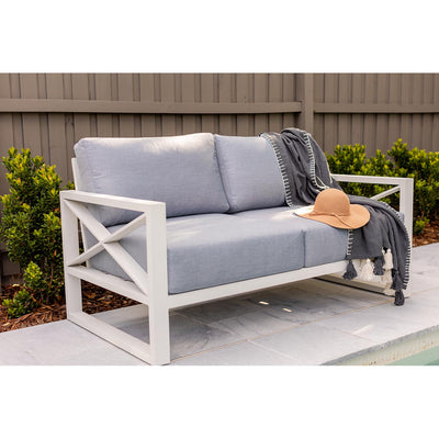 Aluminium outdoor furniture from Linear Lounge collection, featuring a 2-seater outdoor lounge with white frame and light grey cushions, set against a brown fence with plants.