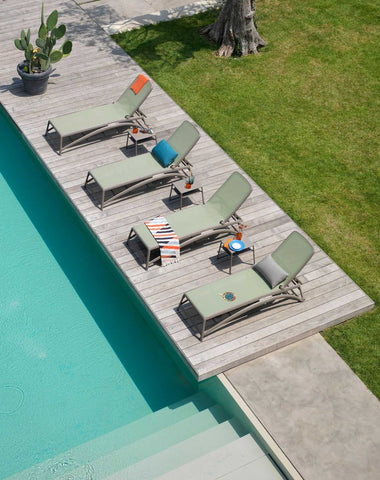 Remarkable Outdoor Living: Nadi Altantico Outdoor Resin Sunlounger. An outdoor pool area is furnished with sleek sun loungers arranged neatly on a wooden deck, complemented by a potted cactus and soft-coloured towels, all inviting relaxation under the open sky.